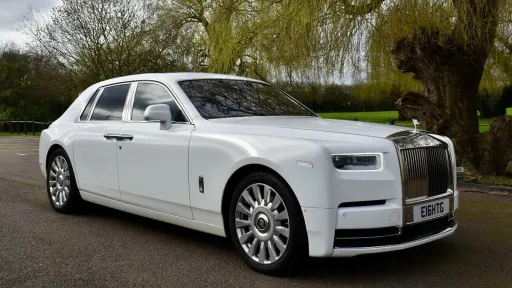 A Modern White Rolls-Royce Phantom 8 with large alloy wheels and chrome grill with the spirit of ecstasy sitting atop