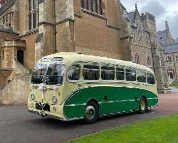 Cream and green classic single decker bus parked outside a stone building