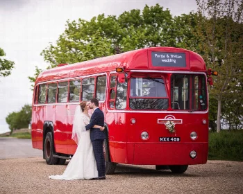 Bride and groom beside a red vintage single decker wedding bus