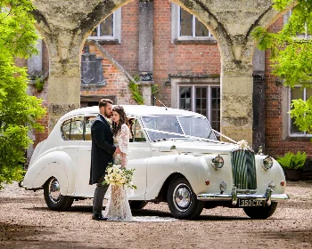 Bride and groom beside a cream Austin Princess limousine decorated with wedding ribbons