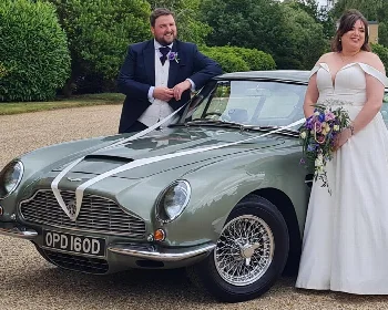 Groom and bride beside a classic Aston Martin DB6 decorated with white wedding ribbons
