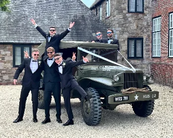 Groom and groomsmen posing with a ribbon-decorated military vehicle
