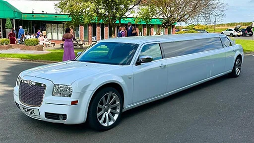 White 8-seater stretched limousine parked at in front of venue with wedding guests in background