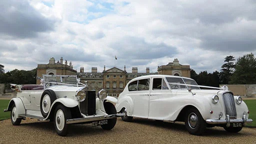White convertible vintage Rolls-Royce parked beside a classic 7-seater classic Austin Princess limousine in white.