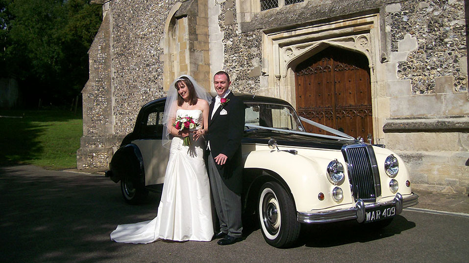 bride and groom with the classic car standing ion front of theior church in uxbridge