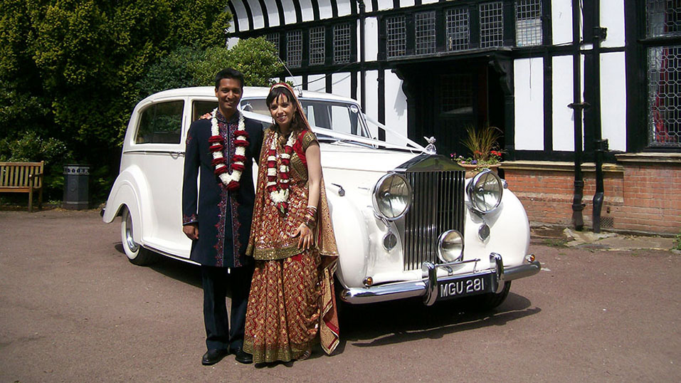 asian couple having photos next to their white vintage rolls-royce