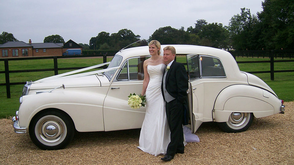bride and groom posing for photo in front of the classic limousine