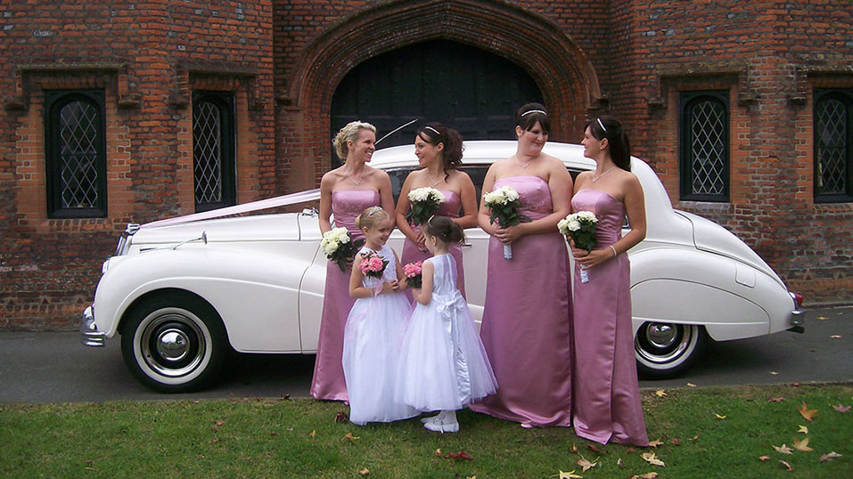 bride and her bridesmaids in front of the classic white car