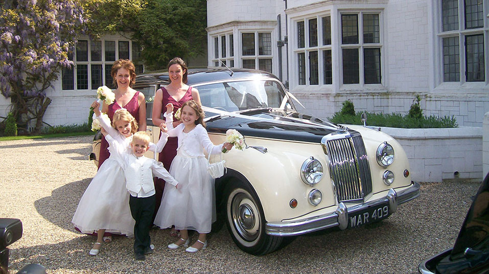bridesmaids, page boy and flower girls in fron to fthe classic car