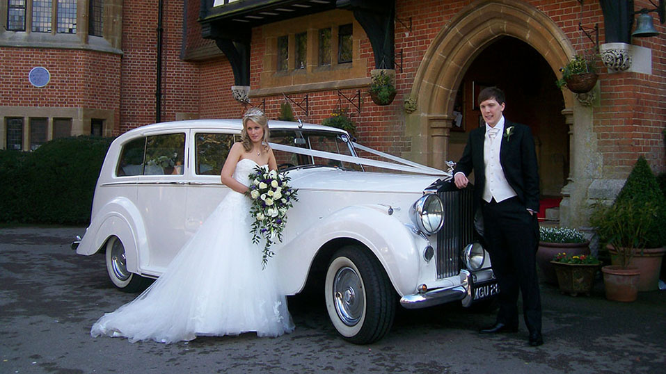 bride and groom having photos with the vintage rolls-royce they've hired