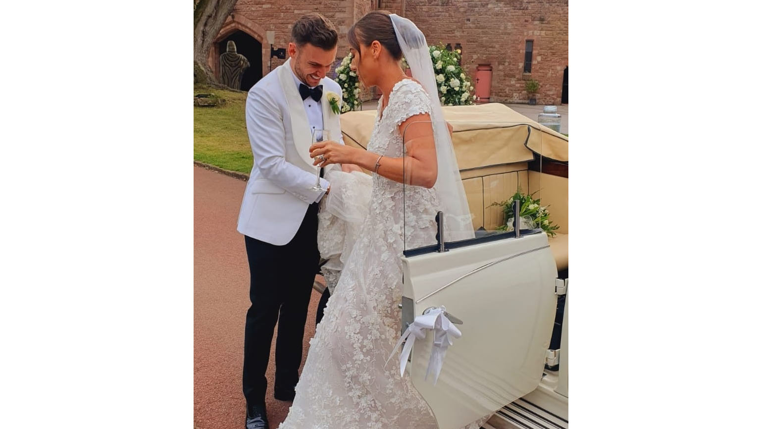 Groom helping Bride out of the convertible classic car hired in front of Peckforton Castle in Cheshire