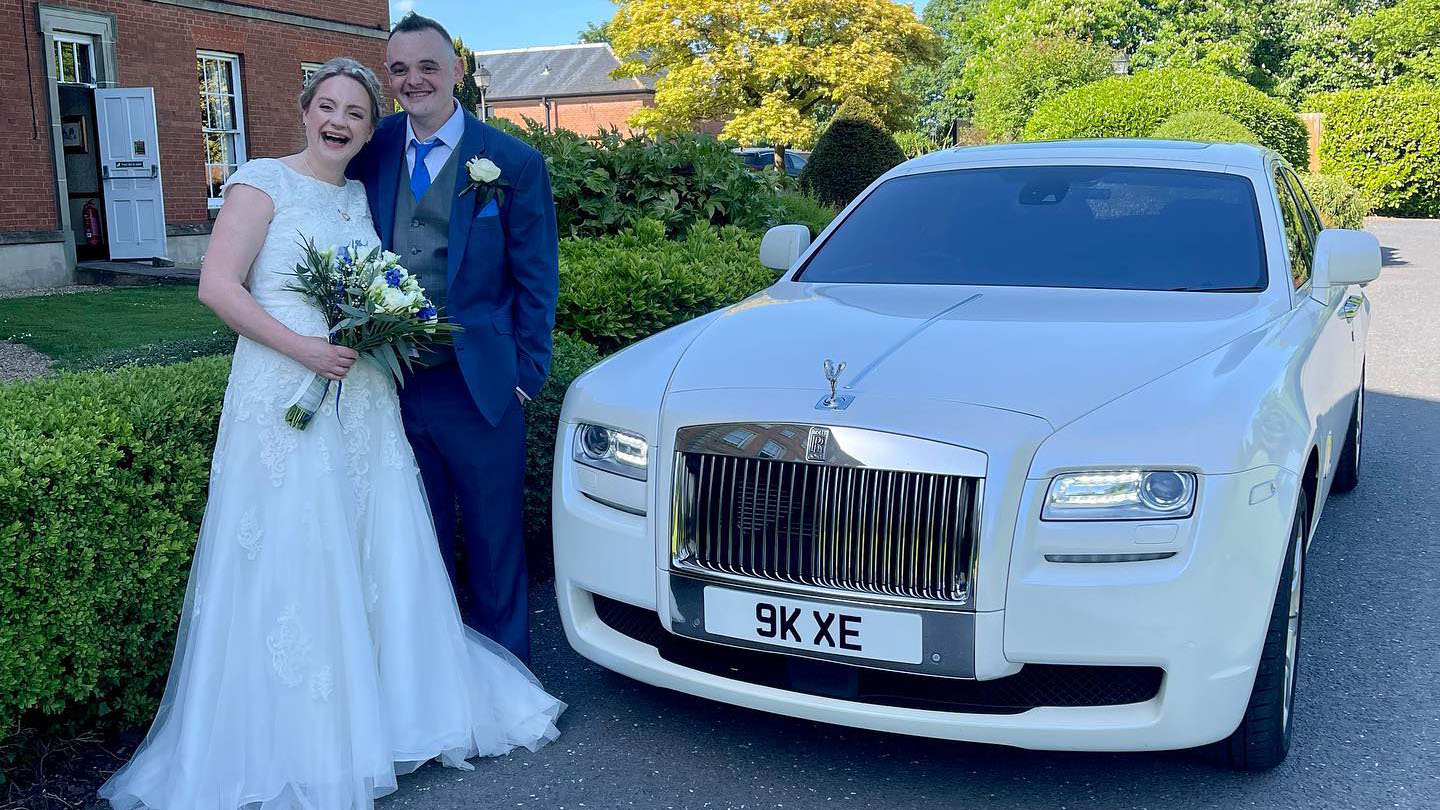 Happy couple standing next a modern white Rolls-Royce after their wedding ceremony