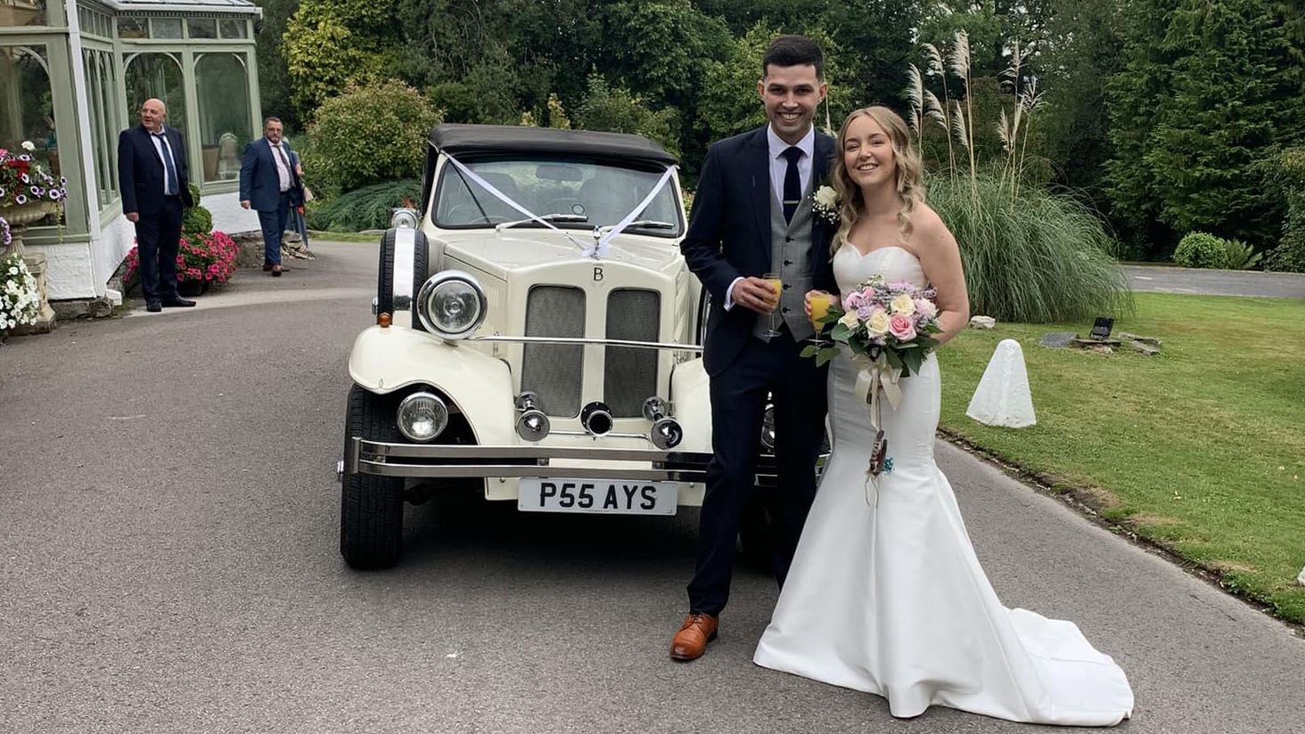 Bride with her bridal bouquet being photographed by the vintage wedding car with her Groom 