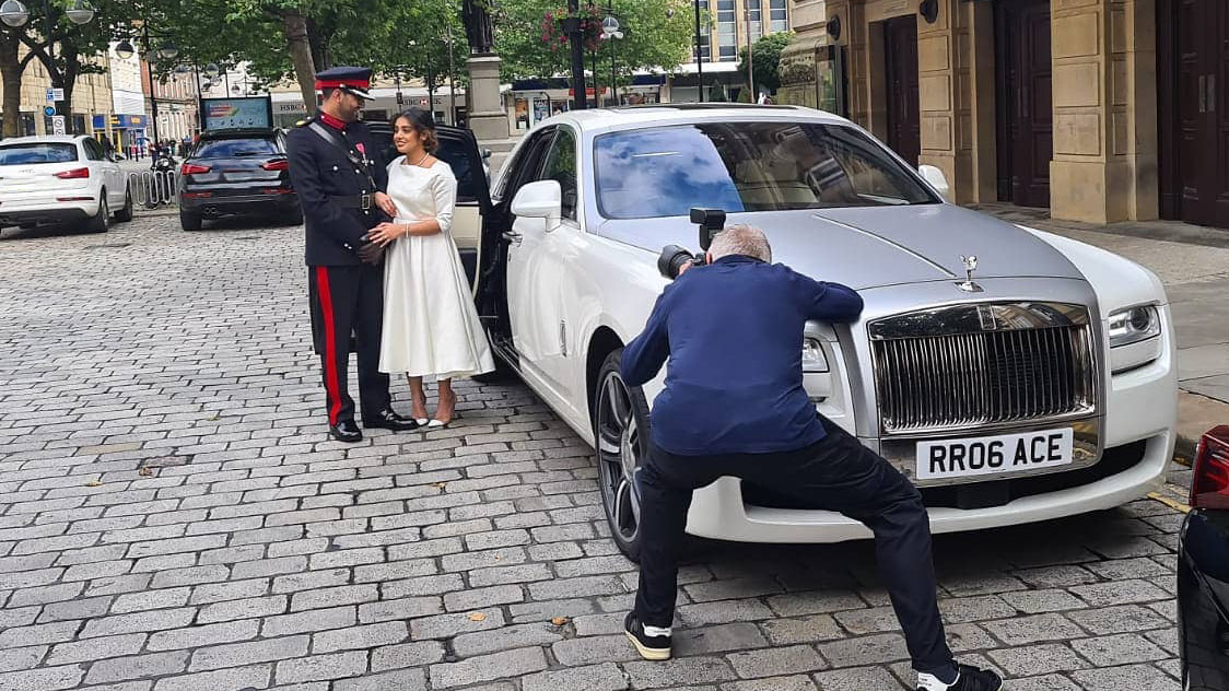 Bride and Groom having photos taken by their photographer by the Rolls-Royce they've hired