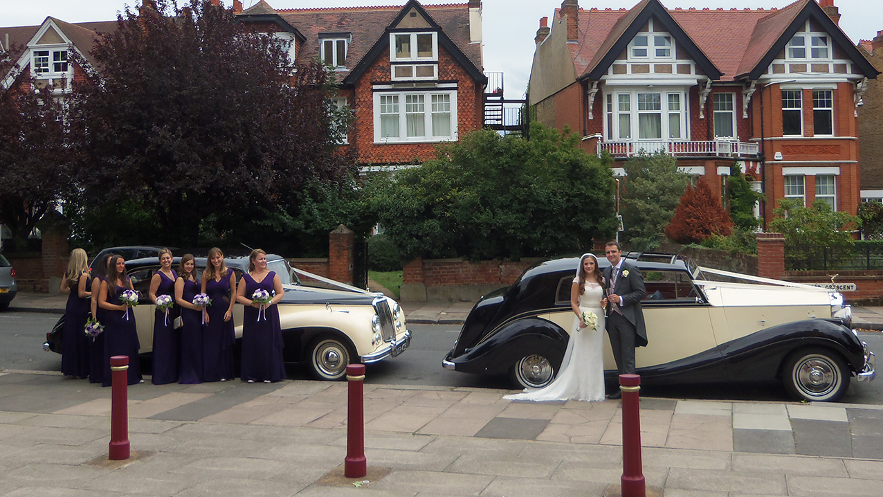 Pair of classic cars with bridemaids in front of them 