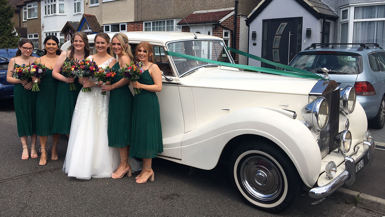 bride and her bridesmaids in front of their white rolls-royce