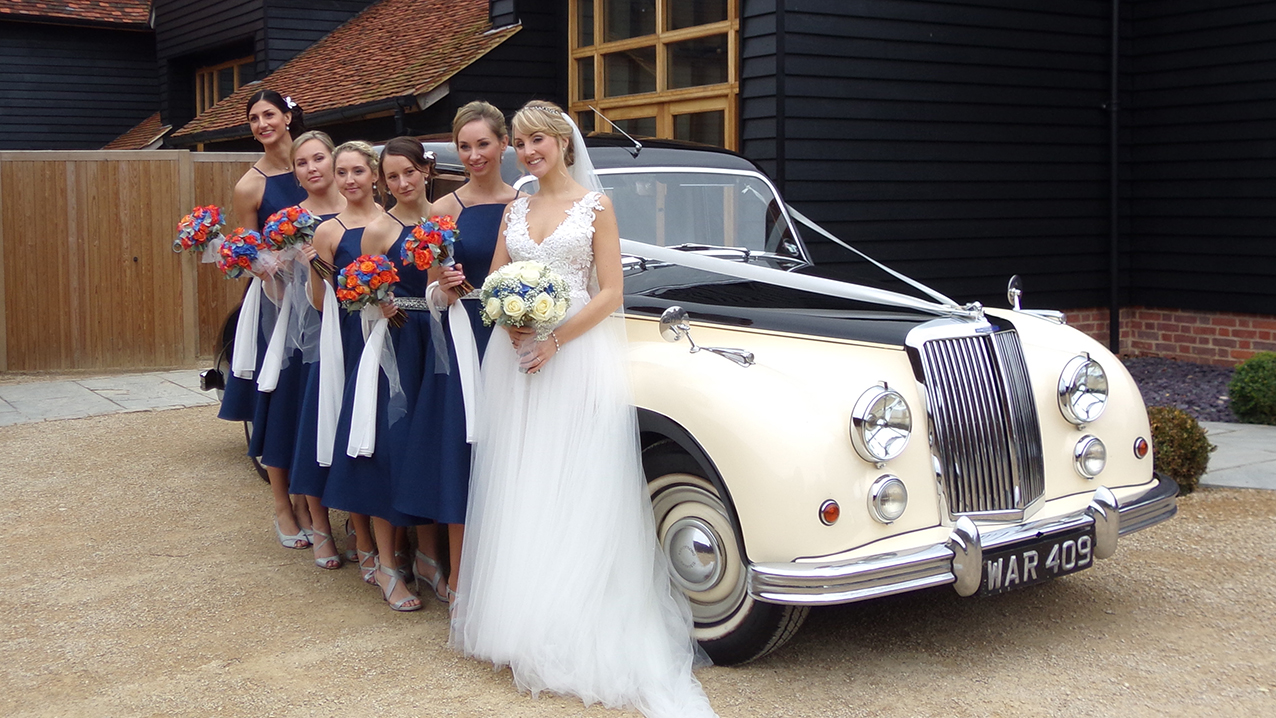 Classic car with bride in her wedding dress and bridesmaids wearing royal blue dresses