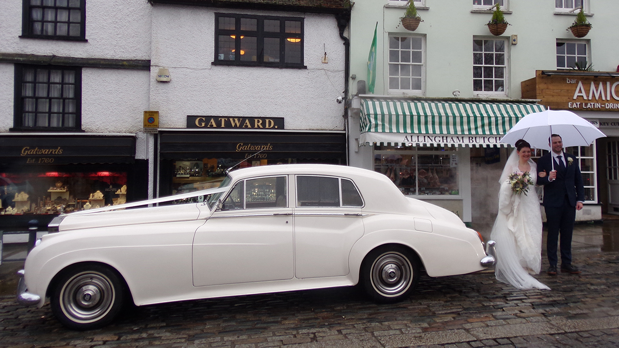 Rolls-Royce Silver Cloud on wedding duty on a rainy day with couple and their large white umbrella