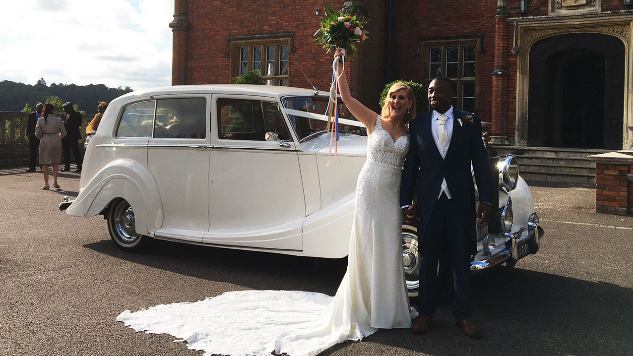 couple standing in front of their wedding cars for photos