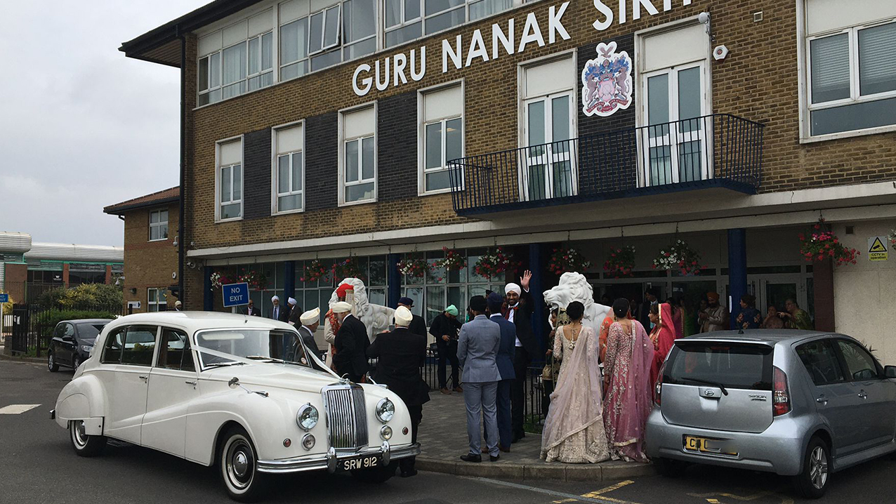 Asian couple with their white classic car in front of the Guru Nanak in West London