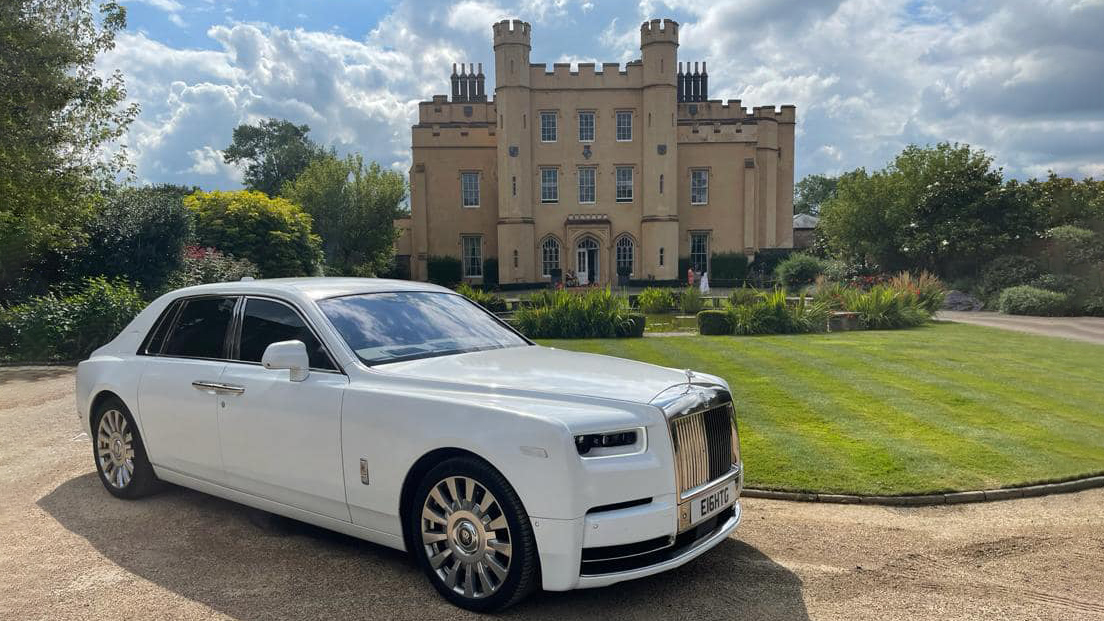 White Rolls-Royce Phantom 8 with its large chrome alloy wheels in attendance at a popular wedding venue. Castle style building in the background.