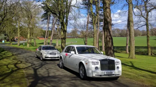 Modern White Rolls-Royce Phantom followed by a White Bentley Flying Spur both dressed with Red bow on the door handling driving through the long entrance at the venue in Powys