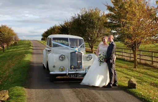 Classic Austin Princess Limousine dressed with baby blue ribbons standing behind the newly wed couple. Bride holds her bridal flowers in her hands