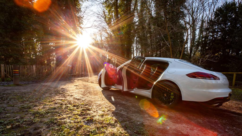 White porsche Hybrid with doors open showing bugundy leather interior taken at sunset