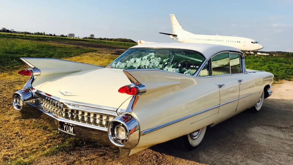 Rear view of a White Cadillac showing fine tail with chrome bumper. Airplane in the background