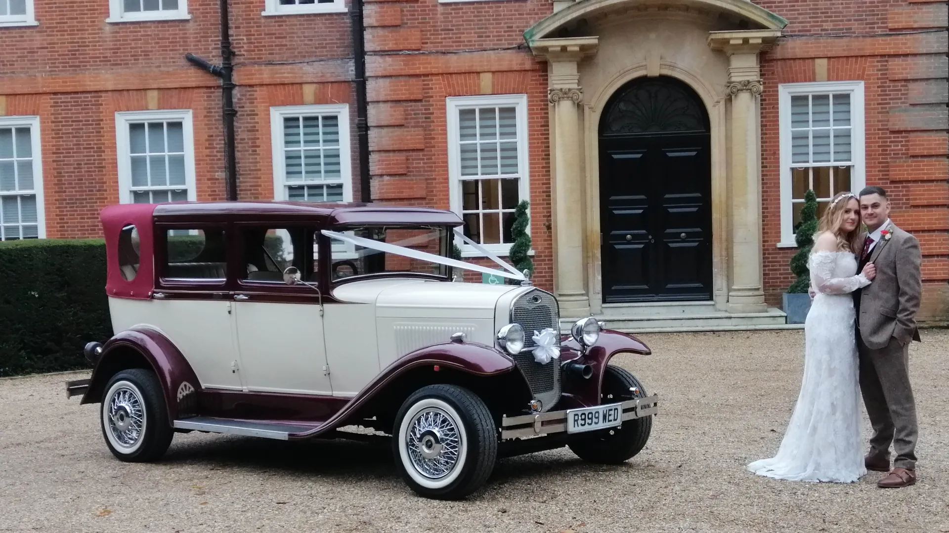 Vintage Badsworth dressed with wedding ribbons in front of wedding venue with Bride and Groom standing next to the vehicle