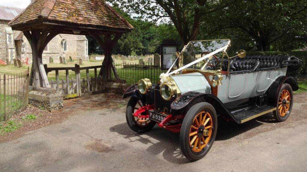 Black & ivory Vintage Oakland with Convertible roof open, dressed with white ribbons, wooden spoke wheels in front of a church