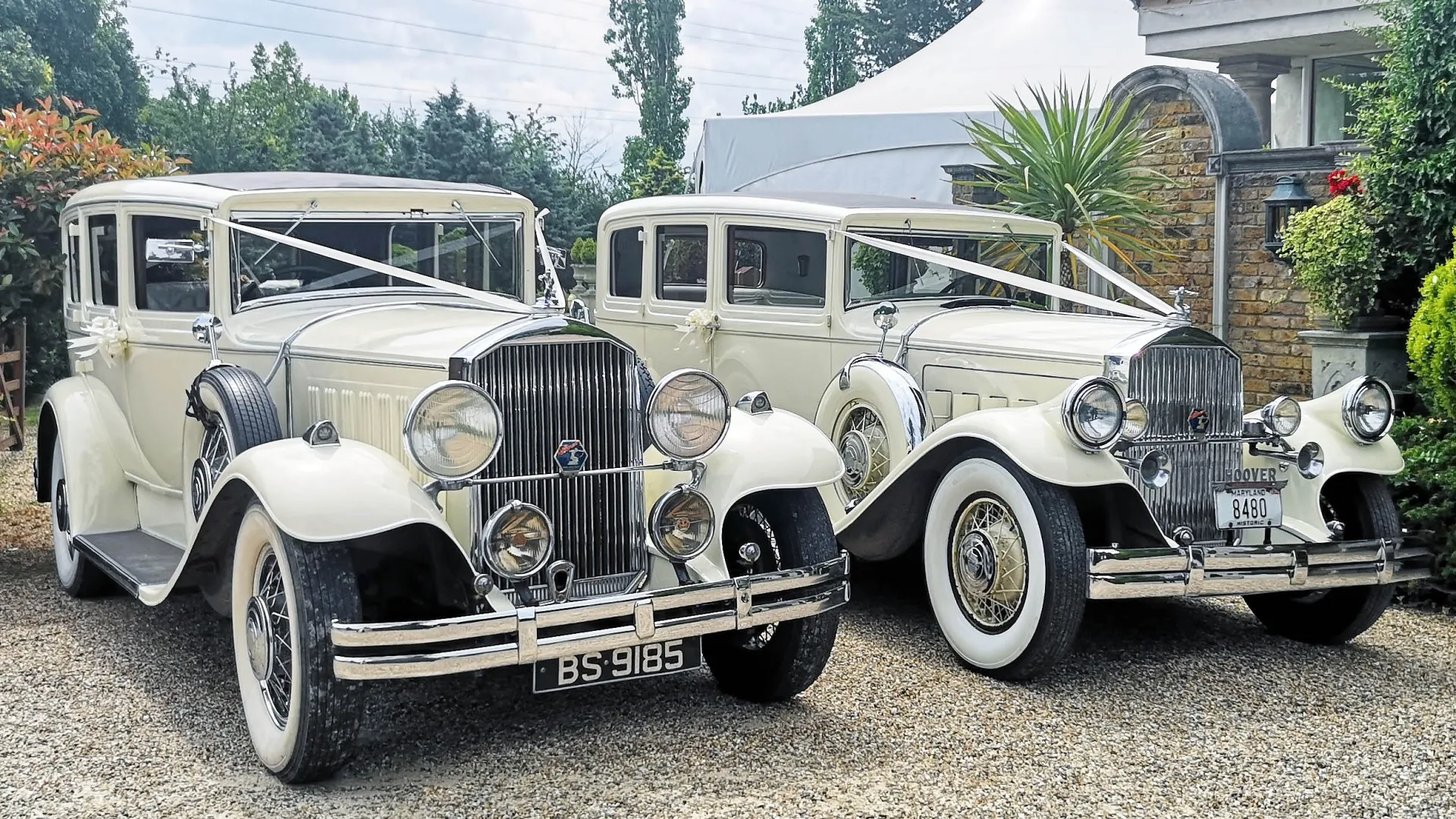 Two Matching Pierce Arrow in front of wedding venue dressed with matching white ribbons