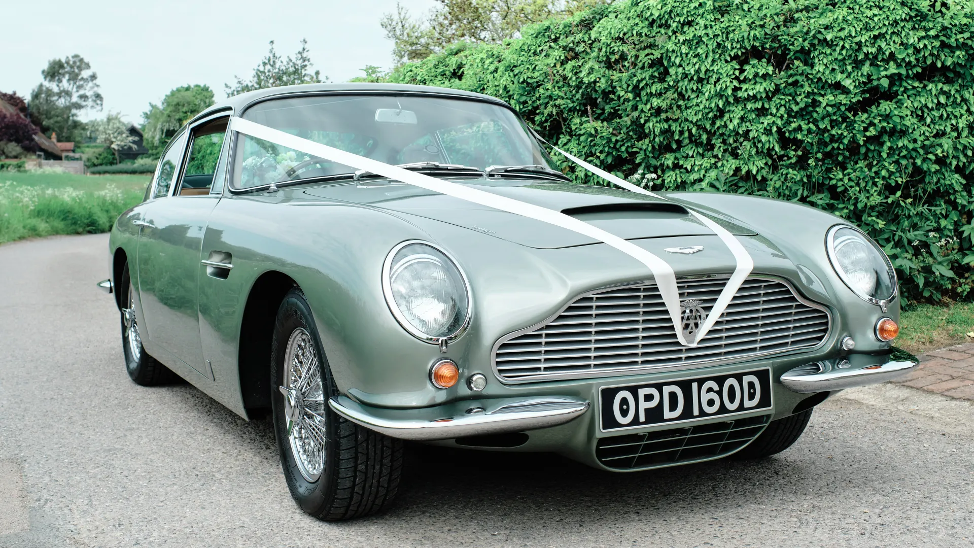 Classic Aston Martin DB6 in Metallic Pale Green dressed with White Wedding Ribbons on its front bonnet