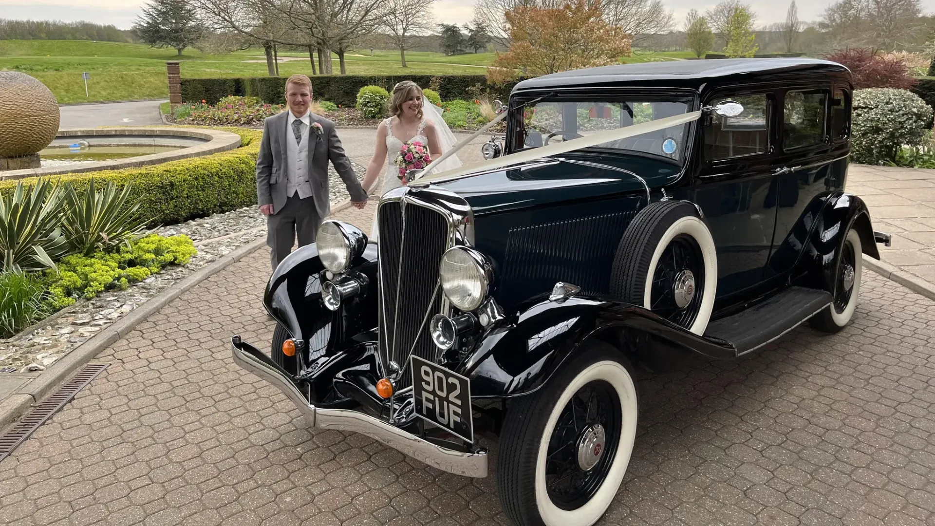 Dark Green Studebaker car dress with white wedding ribbons. Bride and Groom walkking next to the car holding hands