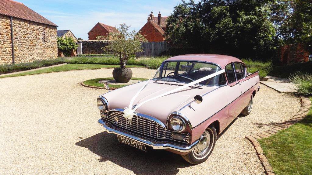 Pink Vauxhall car with white wedding ribbons acrross its front bonnet