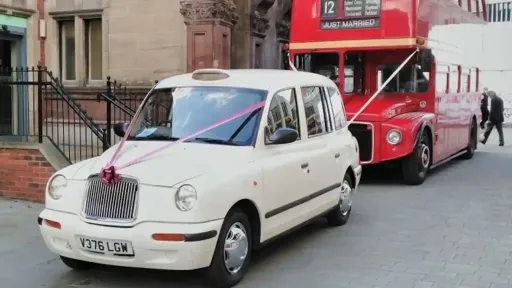 Modern White Taxi Cab decorated with Dark Pink Ribbons followed by a Double Decker Red Routemaster Bus in front of wedding venue