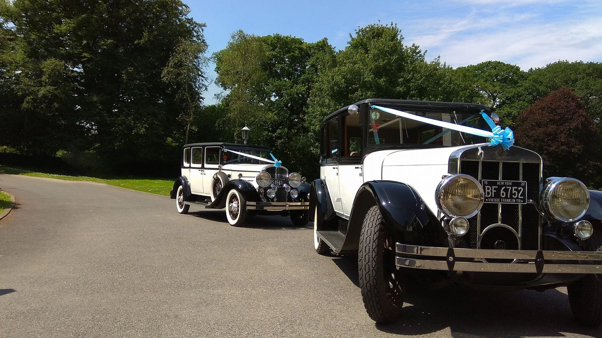 Two matching American Cars with white & blue ribbons in front of a wedding venue