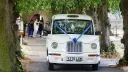 White Modern Taxi Cab entering wedding venue with lilac blue ribbons and bow on front grill