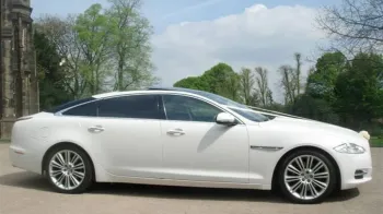 Side view of Jaguar dressed with white ribbons acroos its front bonnet