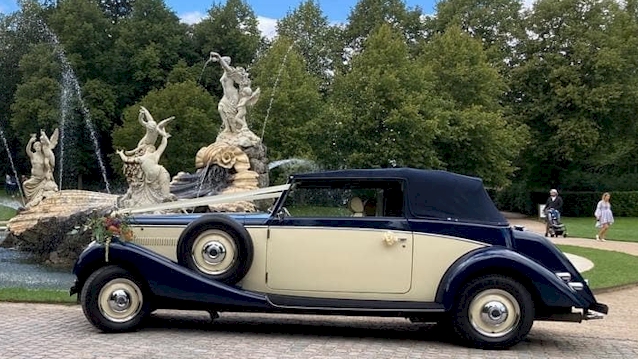 Left side view of vintage car with roof up and white ribbons