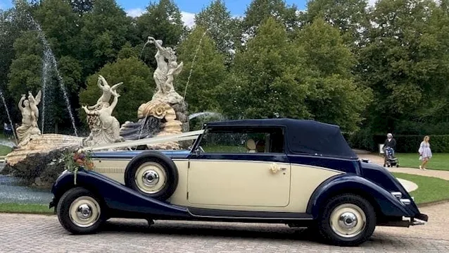 Left side view of vintage car with roof up and white ribbons
