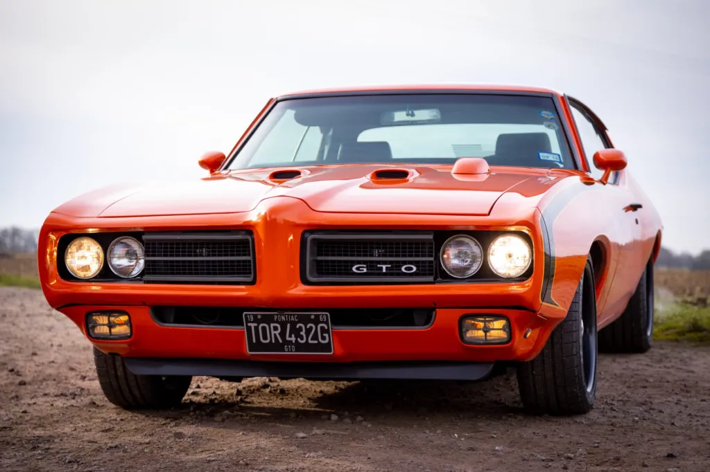Side view of an Orange American Pontiac with Black Stripe and headlights are on