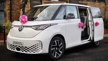 White Electric VW ID Buzz with side rear door open and large Pink bows on the front of the car and door handles