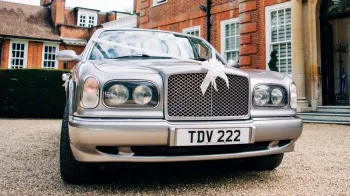 Full front view of silver bentley dressed with Big White Bow on top of the chrome grill