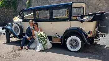 Bride and Groom sitting on the Wheel Arche of a Vintage Bramwith posing for photos. Bride is holding a big Bouquet of flowers