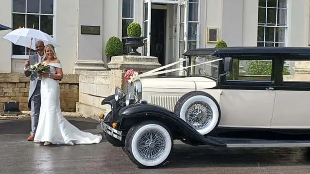Bride and Groom having their photos taken in front of a Vintage BRamwith Limousine. Groom is holding a white umbrella and Bride is holding flowers