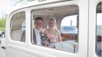Bride and Groom sitting inside the Vintage Daimler. Bride is holding her bridal bouquet