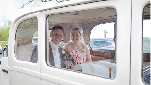 Bride and Groom sitting inside the Vintage Daimler. Bride is holding her bridal bouquet