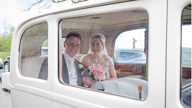Bride and Groom sitting inside the Vintage Daimler. Bride is holding her bridal bouquet