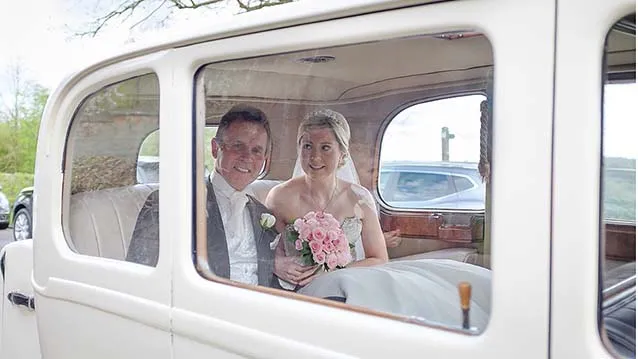 Bride and Groom sitting inside the Vintage Daimler. Bride is holding her bridal bouquet